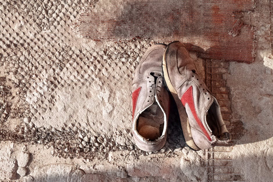 Pair of worn vintage sneakers with red stripes on a textured surface.