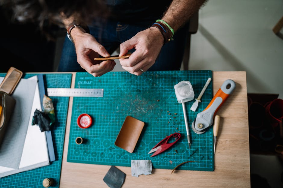 Close-up of hands crafting leather on a workbench. Tools and materials are neatly arranged.