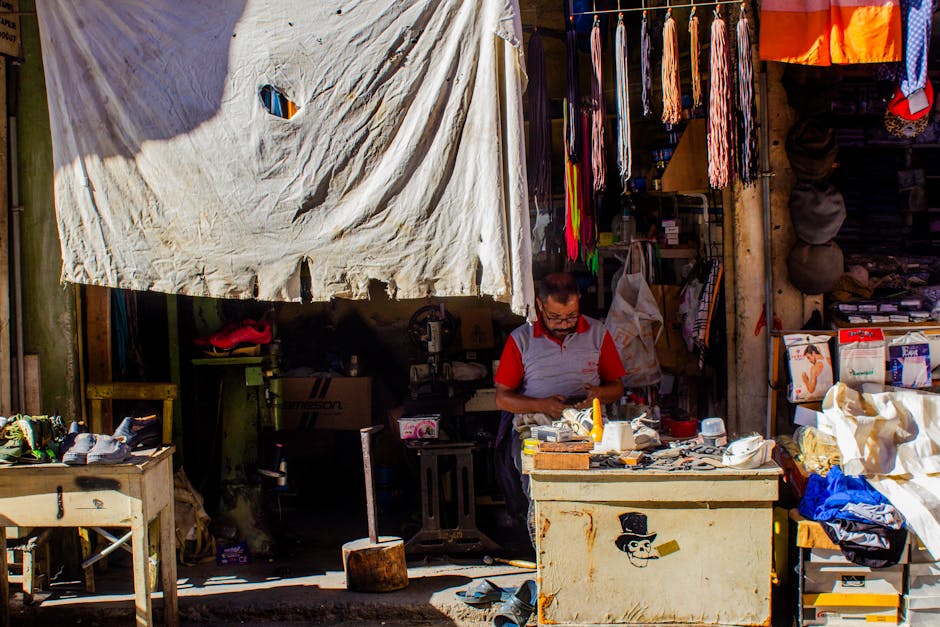 Cobbler working in a traditional shoe repair shop with fabrics and tools.